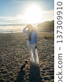 Young woman walking a small cavalier king charles spaniel puppy on a sandy beach during a beautiful golden hour sunset 137309910