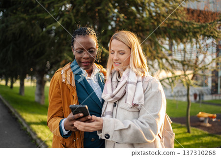 Diverse women friends sharing content on smartphone in park Diverse women friends sharing content on smartphone in park 137310268