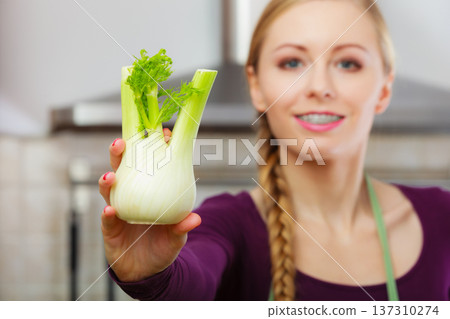 Woman in kitchen holds raw fennel bulb vegetable 137310274