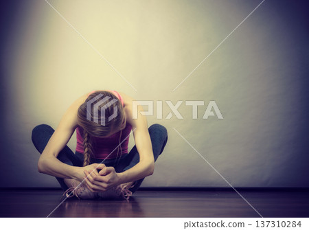 Sad depressed young teenage girl sitting by wall Sad depressed young teenage girl sitting by wall 137310284