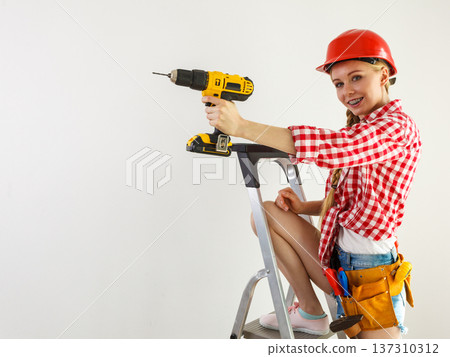 Woman using drill on ladder Woman using drill on ladder 137310312