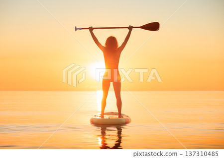 Young woman walking on stand up paddle sup boards by the sea during summer vacation Young woman walking on stand up paddle sup boards by the sea during summer vacation 137310485