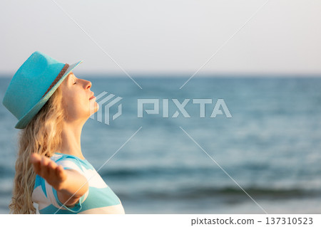 Young happy woman enjoying by sunrise against blue sea and sky on summer vacation Young happy woman enjoying by sunrise against blue sea and sky on summer vacation 137310523