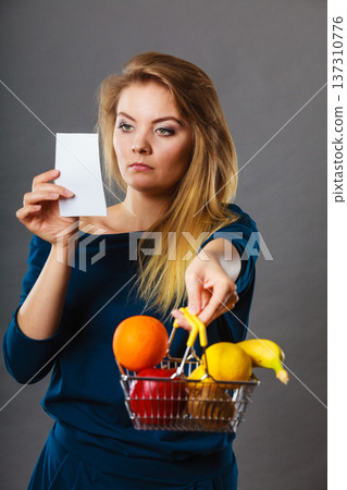 Worried woman holding shopping basket with fruits Worried woman holding shopping basket with fruits 137310776