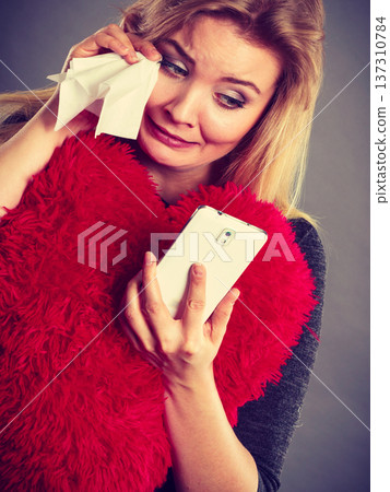 Sad heartbroken woman looking at her phone Sad heartbroken woman looking at her phone 137310784