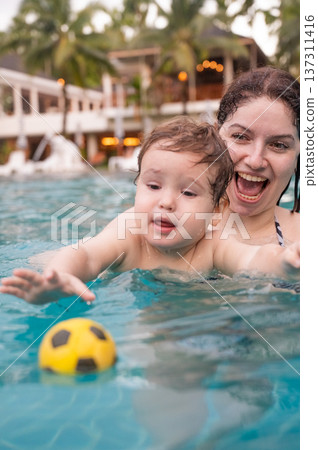 Caucasian woman holds her son while swimming in a pool on vacation. Mom teaches little boy to swim. Caucasian woman holds her son while swimming in a pool on vacation. Mom teaches little boy to swim. 137311416
