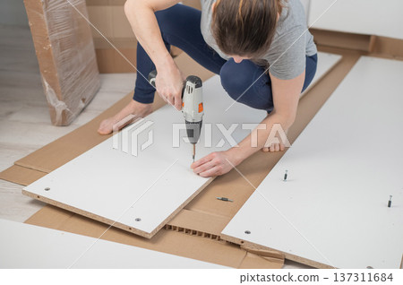 A Caucasian woman uses a screwdriver to tighten a screw while assembling a cabinet. 137311684