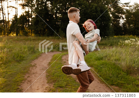 Father Joyfully Carries His Young Daughter Through Vibrant Sunny Meadow Filled With Smiles Father Joyfully Carries His Young Daughter Through Vibrant Sunny Meadow Filled With Smiles 137311803