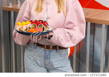 A woman holds a plate of assorted sushi rolls 137311860