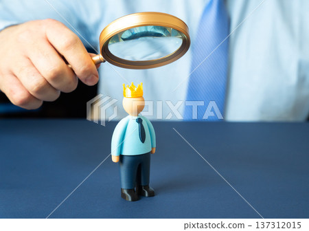 A businessman studies an employee wearing a crown. The concept of leadership and narcissism exploring power ambition authority and workplace psychology. A businessman studies an employee wearing a crown. The concept of leadership and narcissism exploring power ambition authority and workplace psychology. 137312015