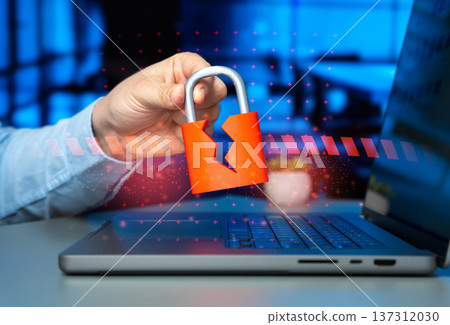 A cracked padlock in a man's hand over a laptop. Hacked security system and corporate data leakage threat highlighting cybersecurity breach and hacker attack risk. 137312030