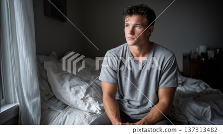 Pensive Young Man Seated on Bed with Crumpled Sheets in Soft Natural Light, Capturing Contemplative  137313482