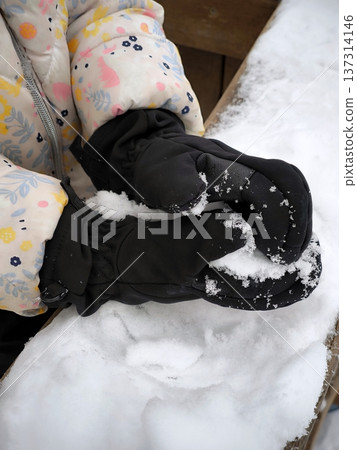 Close-up of children's hands in black mittens playing with snow 137314146