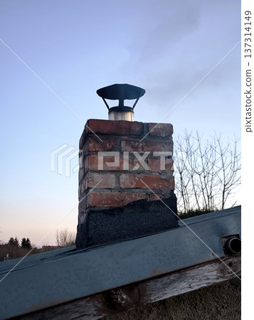 Smoke from a brick chimney against a blue sky, heating a country house or cottage in winter 137314149