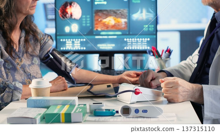 Old expert measuring the blood pressure and tension with a blood pressure monitor, using professional tools at the medical checkup. Physician does a cardiac reading and measurement. Camera B. 137315110