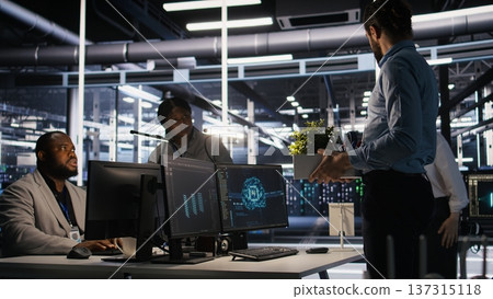 Furious data center engineer packs desk belongings after being replaced by AI automation handling operations. Frustrated man suffering from workforce displacement by artificial intelligence, camera A Furious data center engineer packs desk belongings after being replaced by AI automation handling operations. Frustrated man suffering from workforce displacement by artificial intelligence, camera A 137315118
