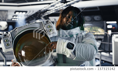 Portrait of happy astronaut holding helmet before stepping out for scheduled operations outside orbital station. Smiling cosmonaut in spacecraft approaching distant planetary surface 137315142
