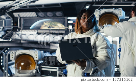 Astronaut monitoring system diagnostics on laptop during human expansion in space mission. Cosmonaut operating spacecraft control interface during mankind survival expedition Astronaut monitoring system diagnostics on laptop during human expansion in space mission. Cosmonaut operating spacecraft control interface during mankind survival expedition 137315162