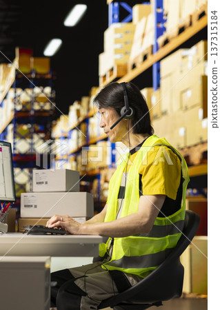 Call center male worker answer help line calls in a logistics warehouse, updating clients on orders and resolving cargo mix ups. Managing shipping software tied to barcodes and airway bills. Call center male worker answer help line calls in a logistics warehouse, updating clients on orders and resolving cargo mix ups. Managing shipping software tied to barcodes and airway bills. 137315184