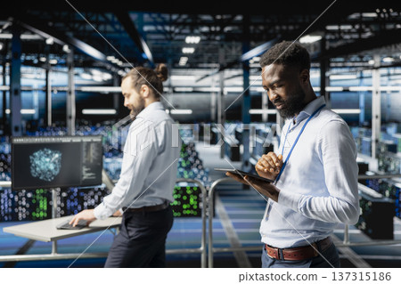 Software engineer next to colleagues reviewing neural network code and LLM visualization dashboards. Data center IT expert monitoring system performance with artificial intelligence tools. Software engineer next to colleagues reviewing neural network code and LLM visualization dashboards. Data center IT expert monitoring system performance with artificial intelligence tools. 137315186