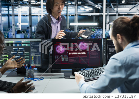 Manager supervising server farm admins alerted by hack warning, securing systems from cyberattack accessing confidential data. Teamworking data center colleagues defending rigs during security breach Manager supervising server farm admins alerted by hack warning, securing systems from cyberattack accessing confidential data. Teamworking data center colleagues defending rigs during security breach 137315187