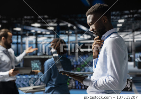 African american expert reviews storage arrays supporting machine learning for system management workflow. Technician on industrial platform handling AI processing tasks, programming. African american expert reviews storage arrays supporting machine learning for system management workflow. Technician on industrial platform handling AI processing tasks, programming. 137315207