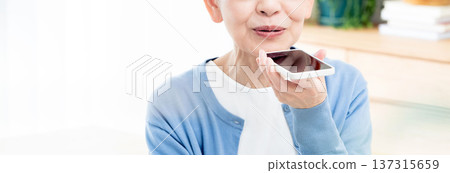 一位老年婦女正在對著智慧型手機說話 137315659