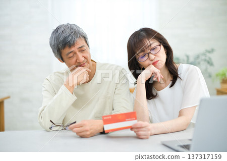 一對六十多歲的夫婦正在客廳裡查看他們的儲蓄存摺。 一對六十多歲的夫婦正在客廳裡查看他們的儲蓄存摺。 137317159
