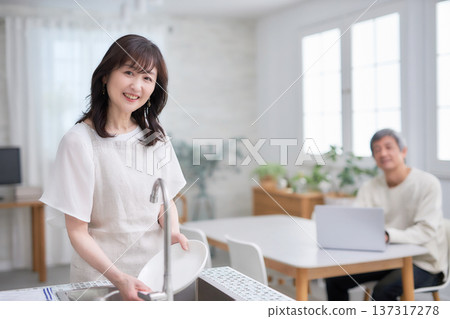 A man and woman in their 60s smiling and talking while wiping dishes in the kitchen A man and woman in their 60s smiling and talking while wiping dishes in the kitchen 137317278