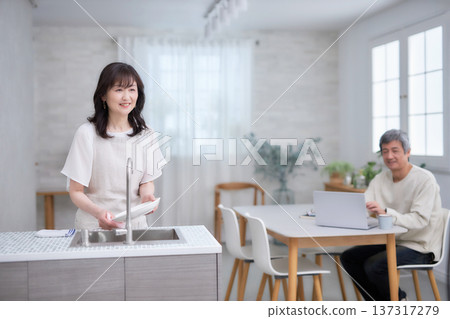 A man and woman in their 60s smiling and talking while wiping dishes in the kitchen A man and woman in their 60s smiling and talking while wiping dishes in the kitchen 137317279