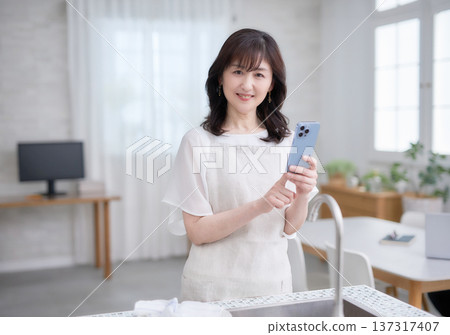 一位六十多歲的婦女在廚房裡看著她的智慧型手機。 一位六十多歲的婦女在廚房裡看著她的智慧型手機。 137317407