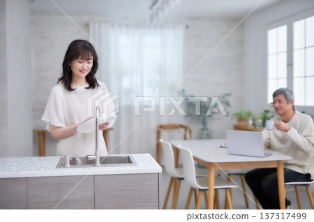 A man and woman in their 60s smiling and talking while wiping dishes in the kitchen 137317499