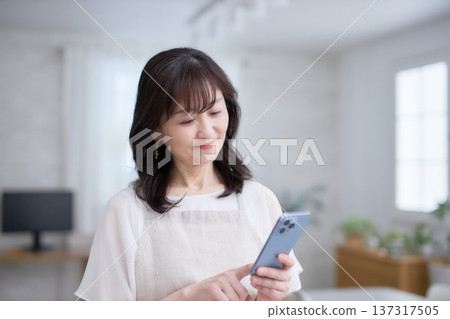 A woman in her 60s looking at her smartphone in the kitchen A woman in her 60s looking at her smartphone in the kitchen 137317505