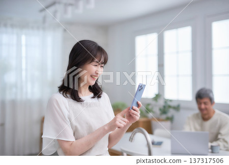 一位六十多歲的婦女在廚房裡看著她的智慧型手機。 137317506