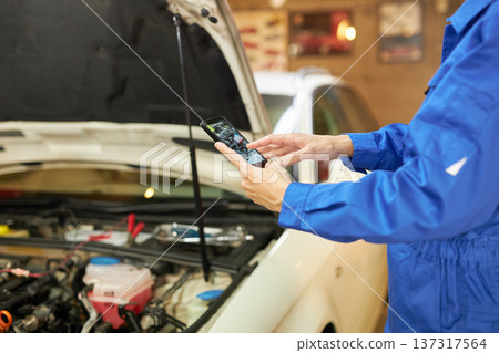 Auto mechanic taking a photo of the inside of the hood with a smartphone Auto mechanic taking a photo of the inside of the hood with a smartphone 137317564