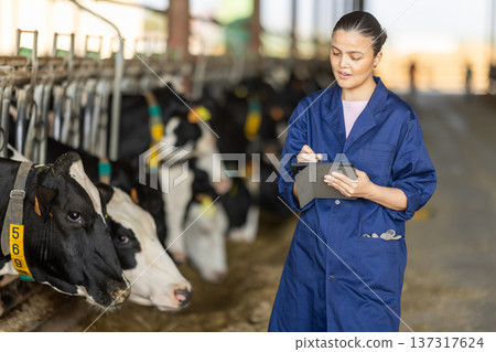 Asian woman working as a veterinarian in a cowshed and taking notes on a tablet Asian woman working as a veterinarian in a cowshed and taking notes on a tablet 137317624