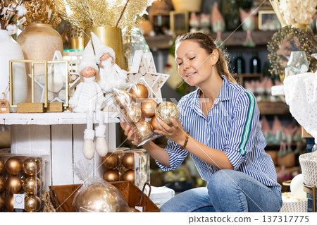 Cheerful lady in casual shirt buying Christmas bulbs before holidays in a store Cheerful lady in casual shirt buying Christmas bulbs before holidays in a store 137317775