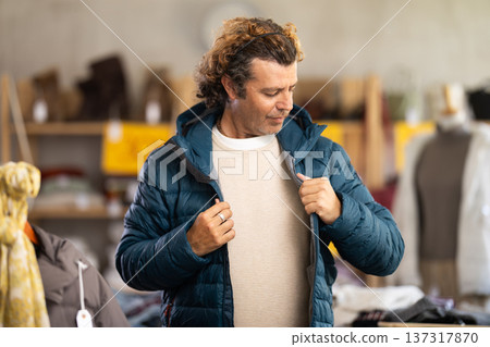Stylish man standing in clothing shop and trying new down jacket 137317870