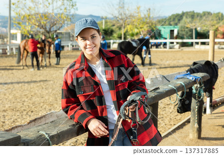 Portrait of female owner of horse farm shows her farm against the backdrop of corral for walking horses Portrait of female owner of horse farm shows her farm against the backdrop of corral for walking horses 137317885
