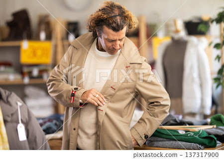 Man try on beige cloak in front of mirror in clothes store Man try on beige cloak in front of mirror in clothes store 137317900