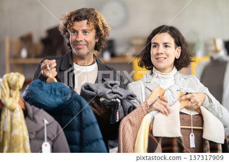 Elegance couple choosing stylish warm coat or down jacket for winter season and posing in clothing boutique Elegance couple choosing stylish warm coat or down jacket for winter season and posing in clothing boutique 137317909