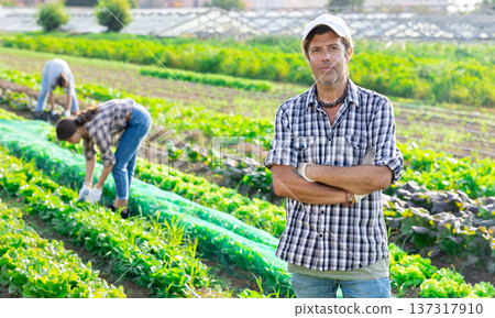 Positive man owner of plantation garden is resting standing after work and tasks. Positive man owner of plantation garden is resting standing after work and tasks. 137317910