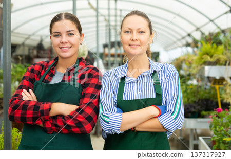 Portrait of two professional female florists standing with crossed hands on chest in greenhouse Portrait of two professional female florists standing with crossed hands on chest in greenhouse 137317927
