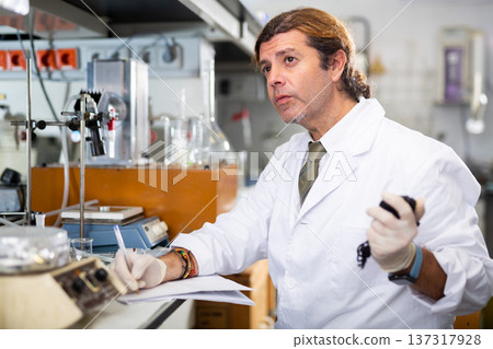 Scientist Latin man writing down result report on paper while analyzing experiment in laboratory Scientist Latin man writing down result report on paper while analyzing experiment in laboratory 137317928