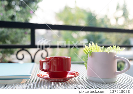 Red coffee cup and stack of notebook on white metal table and pot of fern plant Red coffee cup and stack of notebook on white metal table and pot of fern plant 137318028