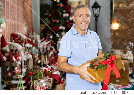 Happy middle-aged man holding a gift box in a store before New Year Happy middle-aged man holding a gift box in a store before New Year 137318073