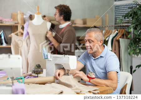 mature woman sews against the background of a tailor and a mannequin mature woman sews against the background of a tailor and a mannequin 137318224