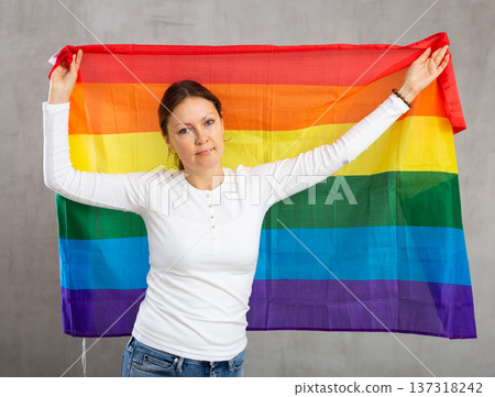 Middle-aged female with serious expression on face standing against gray wall with flag of LGBT Middle-aged female with serious expression on face standing against gray wall with flag of LGBT 137318242