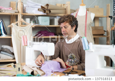 Man tailor sews on sewing machine in workshop Man tailor sews on sewing machine in workshop 137318313