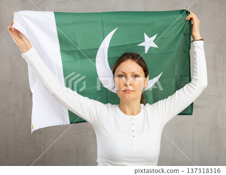 Smiling woman waving flag of Pakistan against gray background Smiling woman waving flag of Pakistan against gray background 137318316